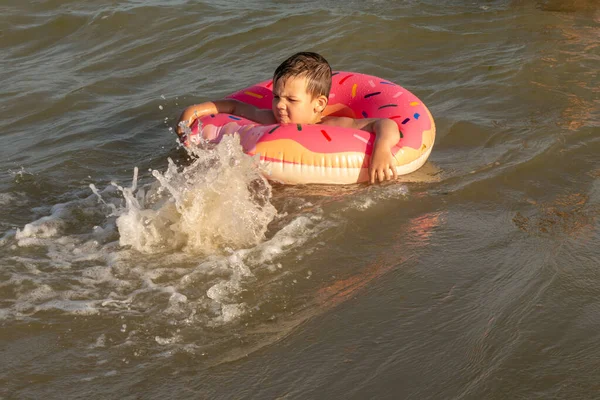 Ein fröhlicher Junge von 5 Jahren schwimmt an einem sonnigen Tag im Meer auf einem aufblasbaren Ring in Form eines Donuts. — Stockfoto