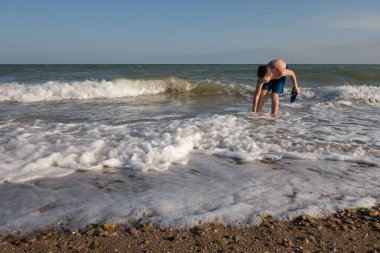 10 yaşında bir çocuk güneşli bir günde deniz kenarında terlik giyer.