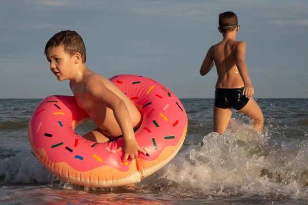 5 ve 10 yaşındaki kardeşler kıyıya yakın denizde yüzüp eğleniyorlar. Donut şeklinde şişme dairesi olan küçük çocuk, yeşil yüzme gözlüklü olan.