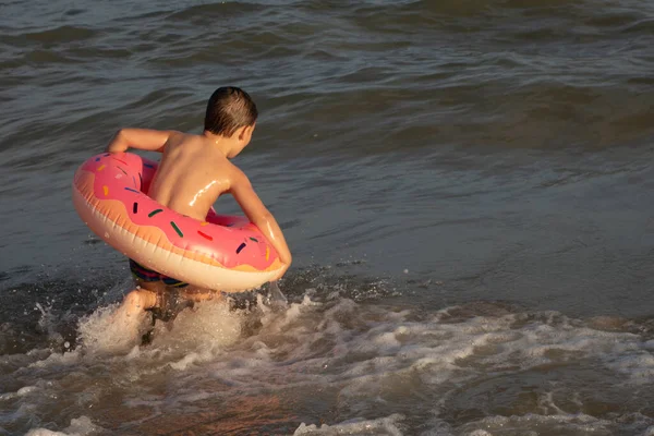一个5岁的男孩在海岸附近的海里游泳 玩的很开心 他有一个甜甜圈形状的充气圈 — 图库照片