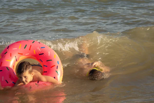 5岁和10岁的兄弟们在海岸附近的海里游泳 玩得很开心 一个年轻的男孩 有一个甜甜圈形的充气圆圈 一个戴着绿色泳镜的大男孩 — 图库照片