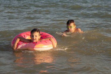 5 ve 10 yaşlarındaki iki kardeş güneşli bir günde denizde yüzer ve eğlenirler.