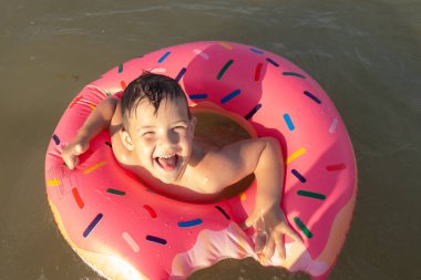 5 yaşında bir çocuk denizde yüzüyor, seviniyor ve çörek şeklinde şişirilebilir bir yüzükle eğleniyor.