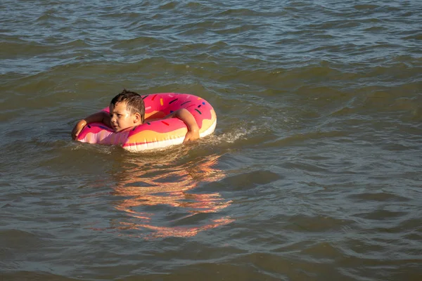 一个5岁的男孩在海里游泳 高兴地在一个充气的圆环里玩乐 圆圈的形状是一个甜甜圈 — 图库照片