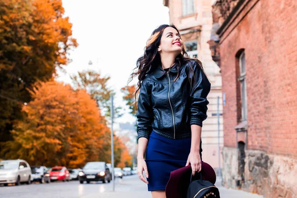 Young fashion woman in casual clothes and black leather jacket over urban city background autumn portrait. Hipster girl posing at street. Fashionable long hair model in elegant autumn clothes.