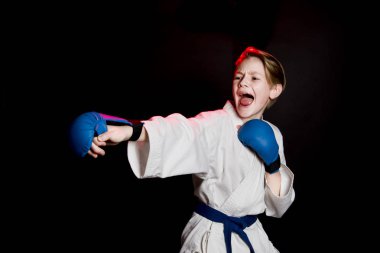 Genç çocuk eğitim karate siyah arka plan üzerine. Mavi kemer ve eldiveni, karate eldiven. Sevimli genç duyguları çocuk eğitim. Şok el ve çığlık.