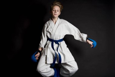 Genç çocuk eğitim karate siyah arka plan üzerine. Mavi kemer ve eldiveni, karate eldiven. Sevimli genç duyguları çocuk eğitim. Şok el ve çığlık.