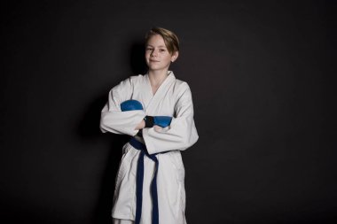 Genç çocuk eğitim karate siyah arka plan üzerine. Mavi kemer ve eldiveni, karate eldiven. Sevimli genç duyguları çocuk eğitim. Şok el ve çığlık.