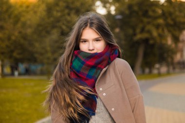 Parkta güzel bir kızın portresi. Genç kız ile renkli atkı ve kahverengi ceket. Fotoğrafı kapatın. Genç öğrenci iyi eğlenceler. Yaşam tarzı fotoğraf. güzel saç.