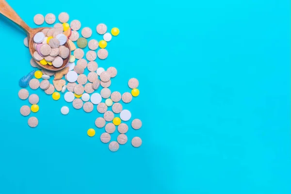 Top view of pharmaceutical medicine pills, capsules and tablets w/ wooden spoon on light blue background. Vitamin and supplement. Health behavior concept. Minimal style. Creative idea.