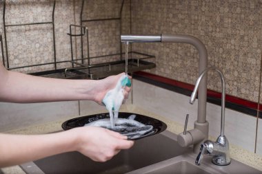 Çocuk lavaboda bulaşıkları yıkıyor.