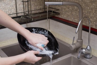 Çocuk lavaboda bulaşıkları yıkıyor.