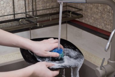 Çocuk lavaboda bulaşıkları yıkıyor.