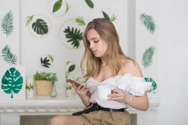 Lindo retrato de joven diseñador y florista, estudiante. Mujer joven bebiendo té sentado en el hermoso interior con flores verdes en el fondo —  Fotos de Stock