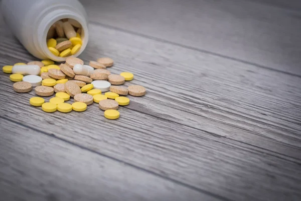 White, yellow and pink pills spilling out of a toppled bright white pill bottle. Medical colorful pills, capsules or supplements for the treatment and health care on wooden background.