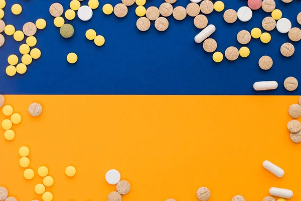 Pillole colorate mediche, capsule o integratori per il trattamento e l'assistenza sanitaria su sfondo blu e arancione o giallo. Idea creativa. Droga. Triste. Muori. Malattia . — Foto Stock