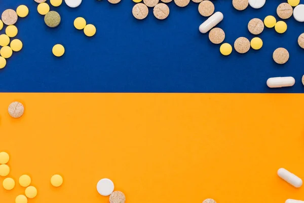 Pillole colorate mediche, capsule o integratori per il trattamento e l'assistenza sanitaria su sfondo blu e arancione o giallo. Idea creativa. Droga. Triste. Muori. Malattia . — Foto Stock