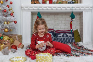Mutlu Noeller ve mutlu tatiller! Şirin küçük kız içeride Noel ağacını süslüyor. Mutlu, küçük, gülümseyen kız Noel hediyesi kutusuyla.