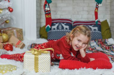 Halıda yatan tatlı küçük kız. Arka planda Noel ağacı var. Gülümsüyor