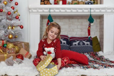 Mutlu Noeller ve mutlu tatiller! Şirin küçük kız içeride Noel ağacını süslüyor. Mutlu, küçük, gülümseyen kız Noel hediyesi kutusuyla.