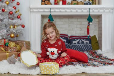 Mutlu Noeller ve mutlu tatiller! Şirin küçük kız içeride Noel ağacını süslüyor. Mutlu, küçük, gülümseyen kız Noel hediyesi kutusuyla.