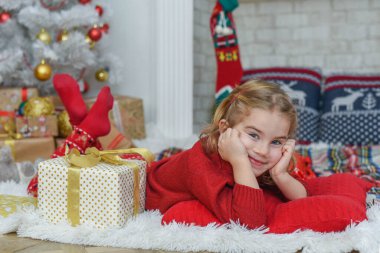 Halıda yatan tatlı küçük kız. Arka planda Noel ağacı var. Gülümsüyor