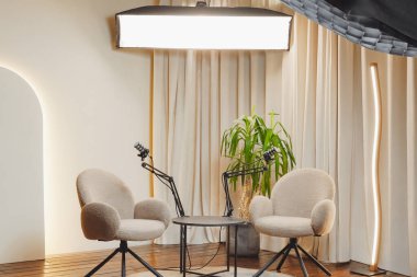 İki yumuşak sandalye ve mikrofon parlak bir podcast stüdyosundaki yuvarlak bir masanın etrafına yerleştiriliyor. Bitkiler uzaya tazelik eklerken büyük bir ışık sabitlemesi atmosferi güçlendirir..