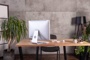 Çağdaş bir ofis kurulumu, minimalist ahşap bir masanın üzerinde yüzeyi buruşmuş kağıtlarla dolu bir bilgisayara sahiptir..