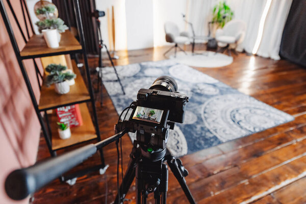 A podcast interview is being prepared with a camera and microphone set up in a warm, inviting room featuring wooden floors and soft lighting.