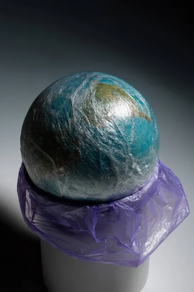 Dünya 'nın bir küresi plastik filmle kaplıdır ve beyaz silindirik bir yüzey üzerinde duran buruşuk bir mor plastik torba içinde oturur. Konsept çevre kirliliğini vurguluyor.