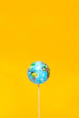 Çubuğun üzerindeki küçük bir küre parlak sarı bir zemin üzerinde belirgin bir şekilde duruyor. Dünya, farklı coğrafya ve kültürlerin yer aldığı farklı ülkeleri vurguluyor..