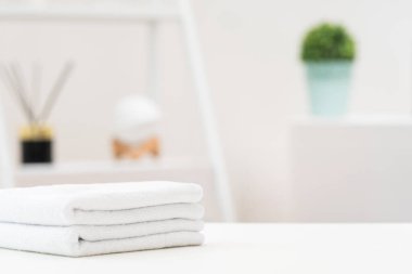 Çağdaş bir odada düzgünce katlanmış beyaz havlular pürüzsüz bir masanın üzerinde duruyor. Yumuşak yeşil bitkiler genel estetiği geliştirmek için sakin ve ferahlatıcı bir atmosfer sağlar..