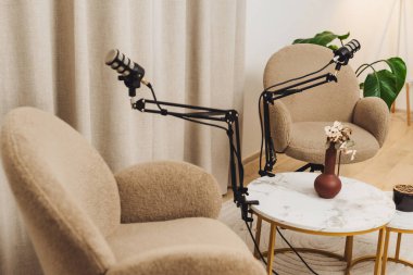 İki rahat stüdyo sandalyesi, her biri ayarlanabilir kollarda profesyonel mikrofonlarla donatılmış küçük mermer bir masaya bakıyor ve podcast kayıtları için davet edici bir alan yaratıyor..