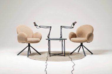 Two soft chairs face each other with microphones attached, creating an inviting space for lively podcast conversations. A small table sits between them, enhancing the cozy atmosphere.