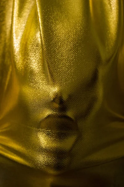 human face pressing through golden fabric