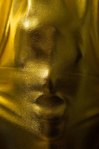 human face pressing through golden fabric