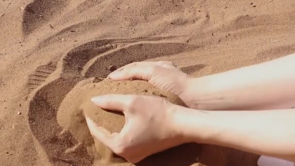 Ziarna piasku przepływają przez żeńskie dłonie. Kobieta trzymająca i uwalniająca piasek przez palce. — Wideo stockowe