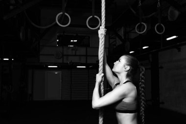 Genç, güçlü, terli, kaslı, çekici ve pozitif güçlü bir kız halata tırmanmaya hazırlanıyor. Gerçek insanların spor salonundan ağır çapraz antrenman eğitimi alıyor.