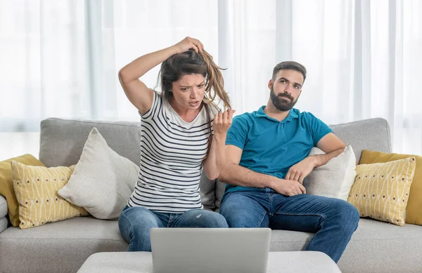 Young guy gets bored while his girlfriend shows her friend online over the laptop how her hairdresser ruined her hair