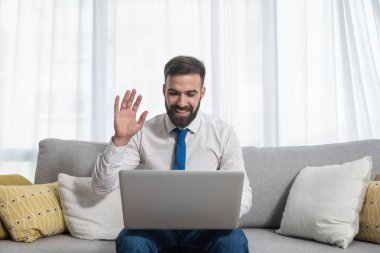 Evde çalışan genç serbest çalışan iş adamı dizüstü bilgisayarla yapılan konferansa merhaba diyor patronuna ve diğer meslektaşlarına yönetici olarak ve yeni projeyi sunmaya hazırlanıyor.