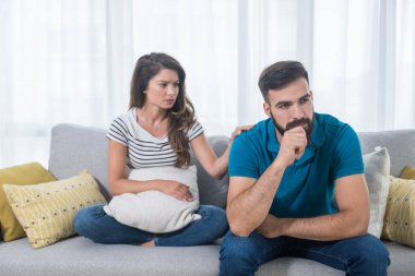 Oturma odasındaki kanepede oturan genç bir çift kız ve erkek tartıştılar ve kız arkadaşının elini erkek arkadaşının omzuna koyduğu yerde konuşmadılar ve onu sakinleştirmeye çalıştılar.