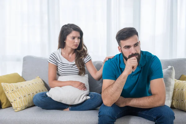 Oturma odasındaki kanepede oturan genç bir çift kız ve erkek tartıştılar ve kız arkadaşının elini erkek arkadaşının omzuna koyduğu yerde konuşmadılar ve onu sakinleştirmeye çalıştılar.