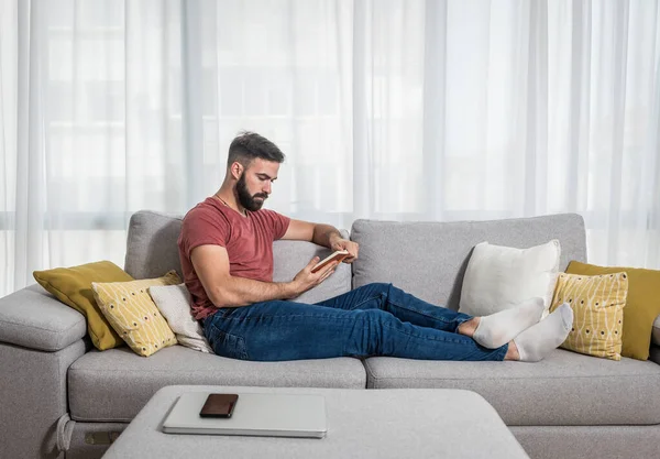 Young beautiful man or guy lying on the sofa at home reading the book and enjoying his free time without his wife and children with smile and happy face