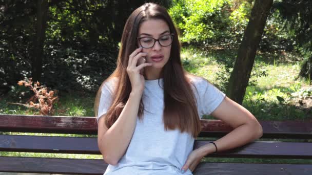 一个漂亮的女孩或女人独自坐在公园的长椅上 与男朋友在手机上交谈和争论 感到沮丧和愤怒 — 图库视频影像