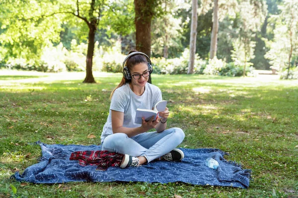 Молода Жінка Сидить Парку Читаючи Книгу Слухаючи Музику Через Бездротові — стокове фото