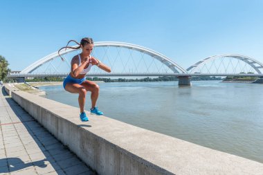 Genç seksi, terli, kaslı, formda bir kadın spor salonunda vücut egzersizi yapmak için duvardan atlıyor.