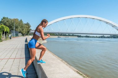 Genç, güçlü, formda, kaslı bir kadın, tek diziyle duvara tırmanıyor ve vücut ağırlığıyla antrenman yapıyor.