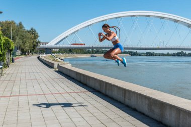 Şortlu, seksi ve formda bir kadın yüksek dizlerle atlıyor. Açık hava sert vücut egzersizi antrenmanı gibi.