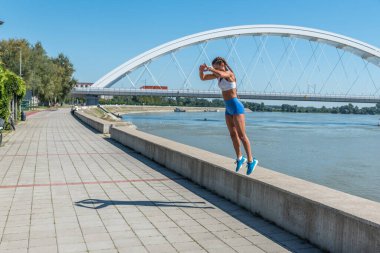 Şortlu, seksi ve formda bir kadın yüksek dizlerle atlıyor. Açık hava sert vücut egzersizi antrenmanı gibi.