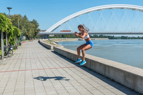 Şortlu, seksi ve formda bir kadın yüksek dizlerle atlıyor. Açık hava sert vücut egzersizi antrenmanı gibi.